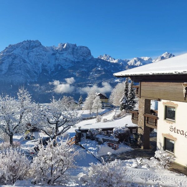Der Bauernhof Straganzhof im Winter, mit Blick auf die verschneiten Berge und den ebenfalls schneebedeckten Kinderspielplatz.