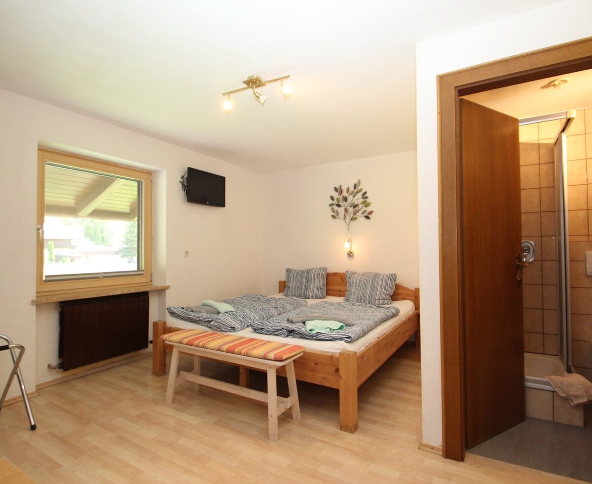 Doppelzimmer im Bauernhof mit Doppelbett, Fenster, Wandfernseher, Kofferablage und eigenem Bad mit Dusche und WC.