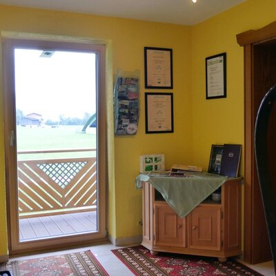 Der Eingangsbereich des Bauernhofs bietet Gästeinformationen, gerahmte Zertifikate und einen Ausgang zu einem Balkon mit Blick auf die Felder.