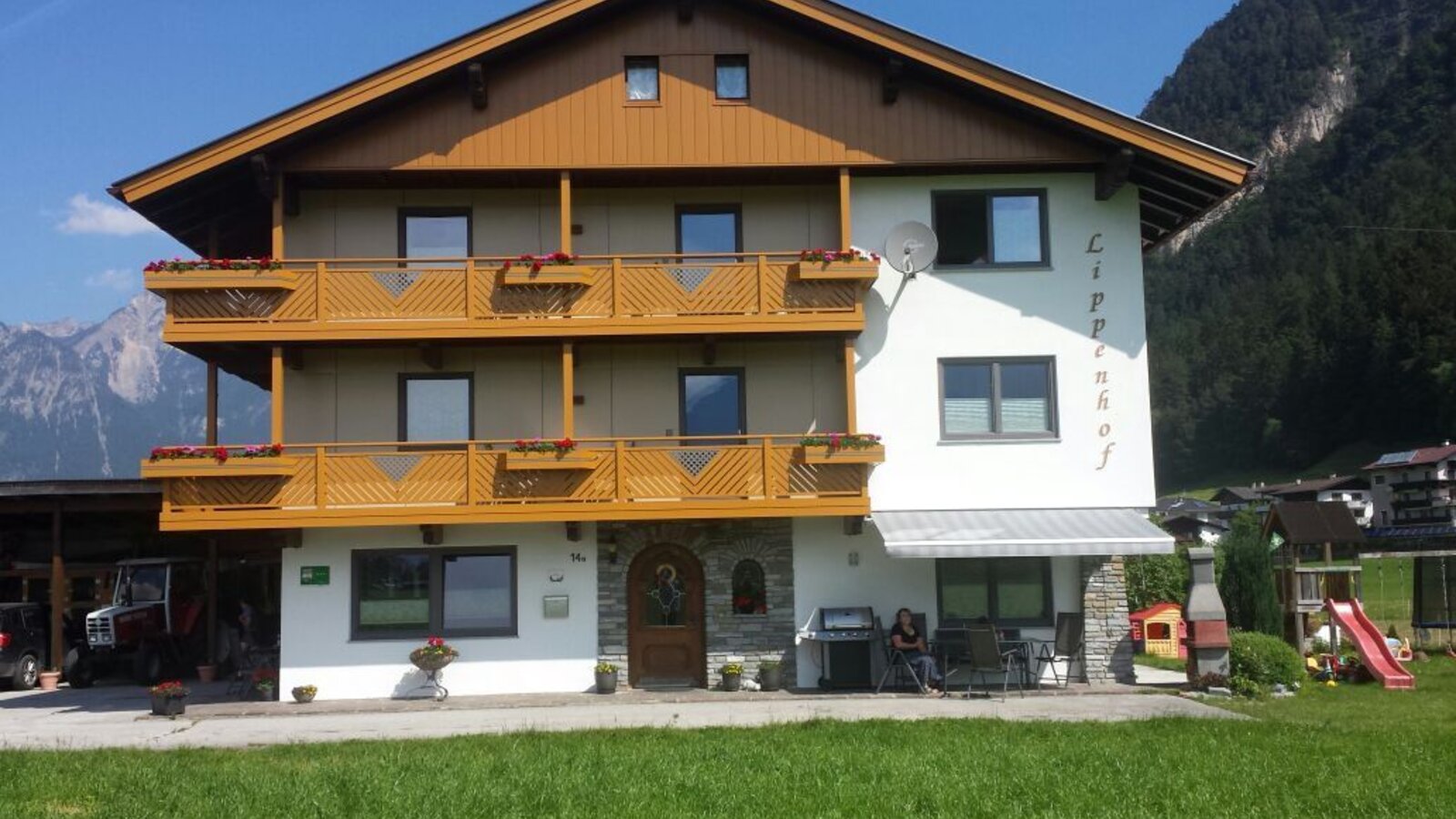 Außenansicht des Bauernhofs mit Holzbalkonen und einem Kinderspielplatz im Gartenbereich.