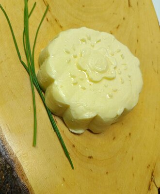 Frisch geformte Bauernhofbutter mit Schnittlauch auf einem Holzbrett.