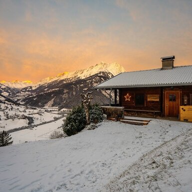 Der Bauernhof in verschneiter Landschaft mit Blick auf die Berge bei Sonnenuntergang.
