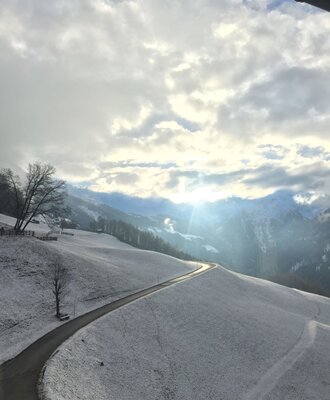 Die winterliche Berglandschaft mit einer Straße und Sonnenstrahlen, sichtbar vom Bauernhof.