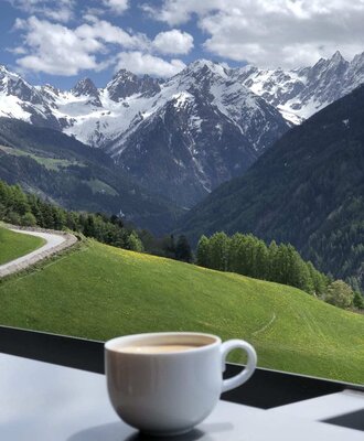 Eine Tasse Kaffee auf dem Balkon des Bauernhofs mit weitem Blick auf die grünen Hänge und schneebedeckten Berggipfel.