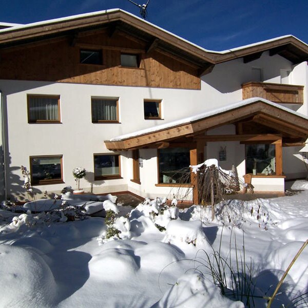 Der Bauernhof mit weißer Fassade, Holzbalkonen und überdachtem Eingangsbereich, umgeben von Schnee.