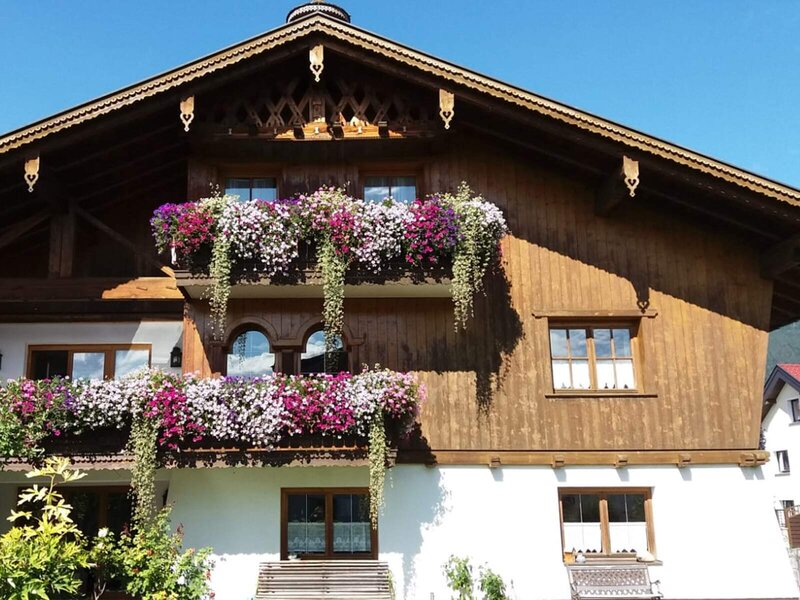 Der Bauernhof mit traditioneller Holzfassade und blühenden Blumenkästen an den Balkonen.