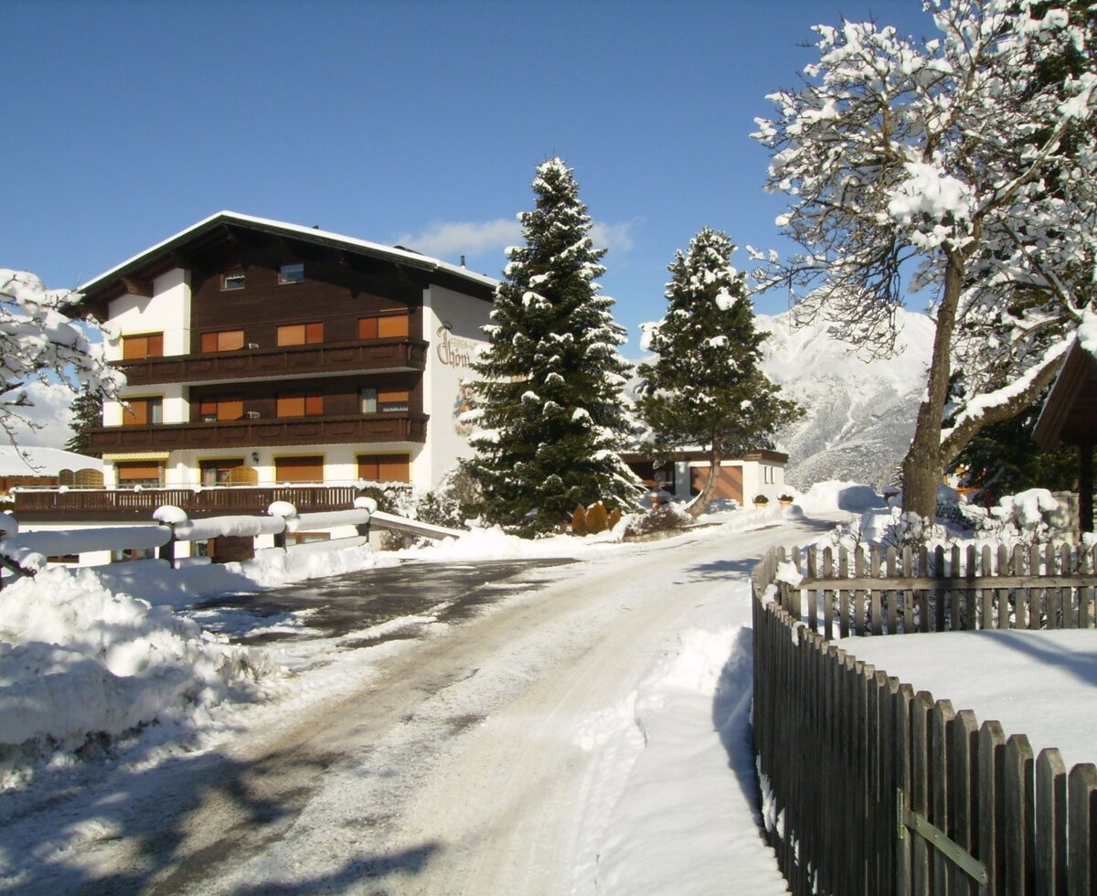 Der Bauernhof in verschneiter Winterlandschaft mit Zugangsweg und Blick auf die Berge.