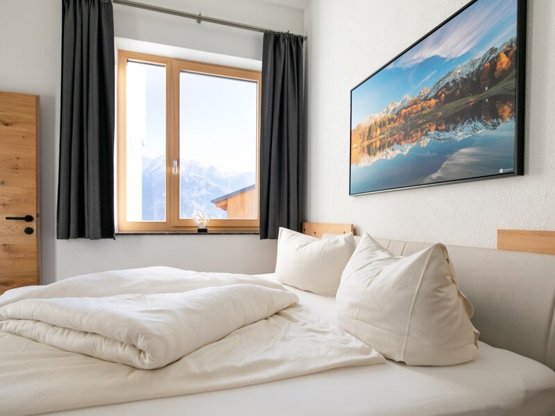 Schlafzimmer der Ferienwohnung mit Doppelbett, Fenster mit Bergblick und Holztür.