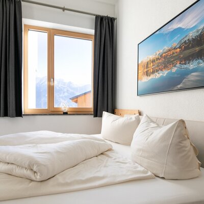Schlafzimmer der Ferienwohnung mit Doppelbett, Fenster mit Bergblick und Holztür.