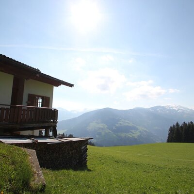 Flecklhütte mit Balkon, gelegen auf einer grünen Wiese mit Blick auf die Berge.