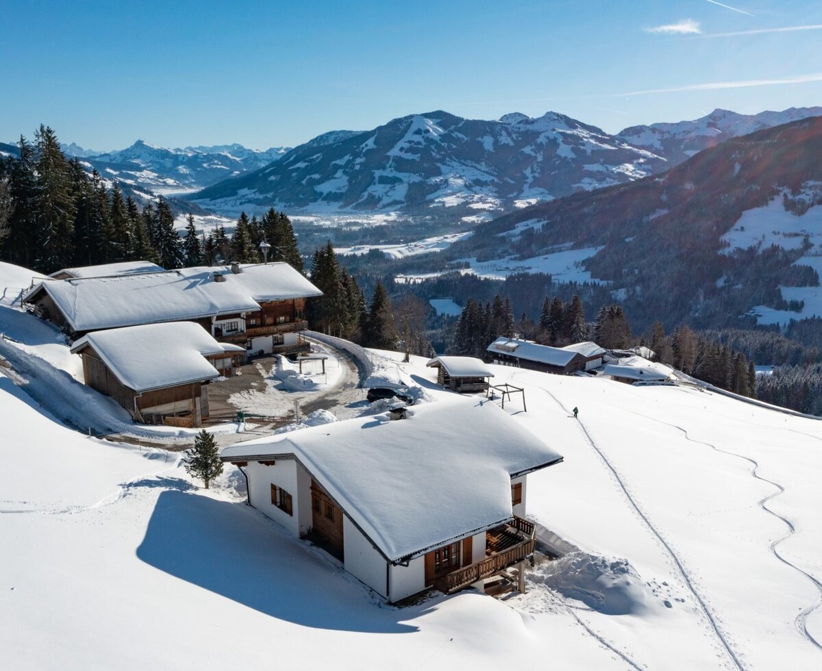 Die Flecklhütte, bestehend aus mehreren schneebedeckten Gebäuden, eingebettet in eine winterliche Berglandschaft.