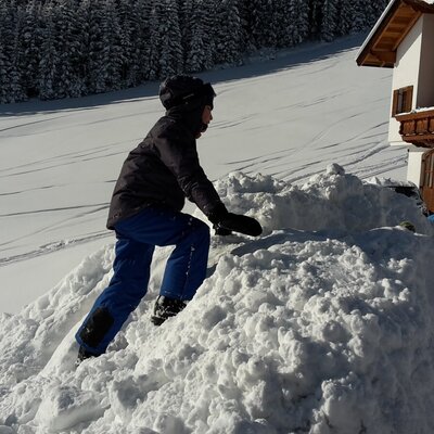 Ein Kind spielt im Winter mit Schnee vor der Alm.