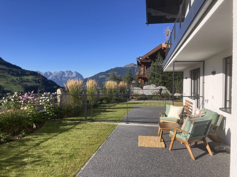 Die sonnige Terrasse des Bed and Breakfasts bietet einladende Sitzgelegenheiten, einen gepflegten Rasen und einen herrlichen Blick auf die umliegenden Berge.
