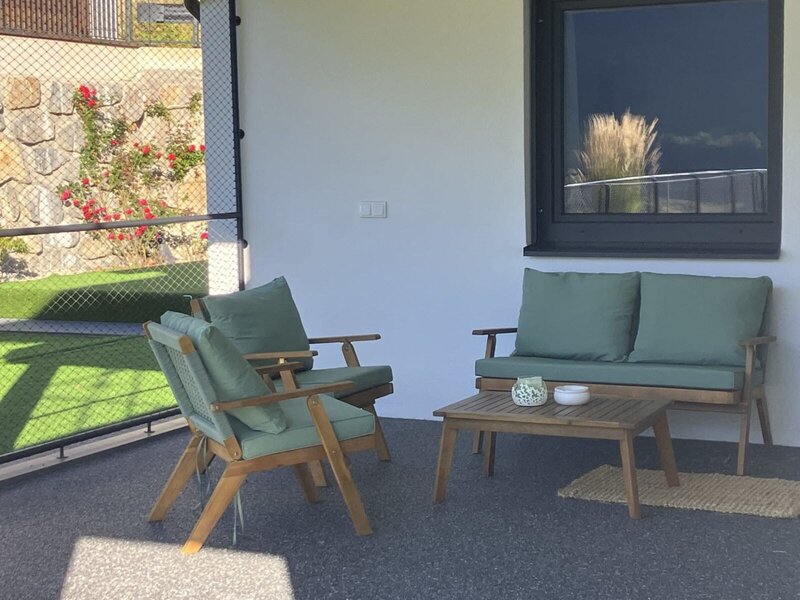 Eine einladende, überdachte Terrasse des Bed and Breakfasts mit gemütlichen Holzmöbeln und grünen Polstern zum Entspannen.