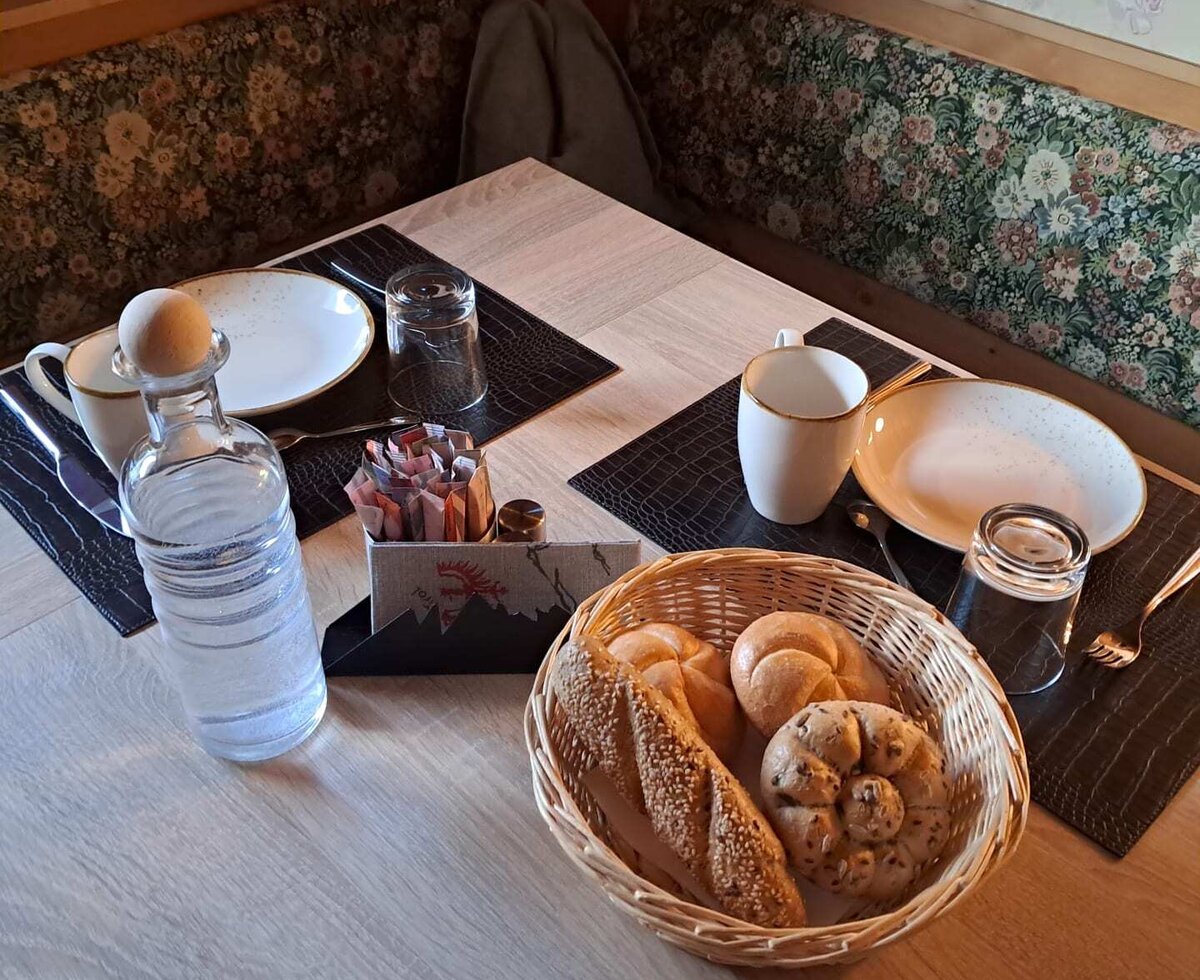 Ein liebevoll gedeckter Frühstückstisch im Bauernhof mit frischen Brötchen und einer gemütlichen Sitzecke.