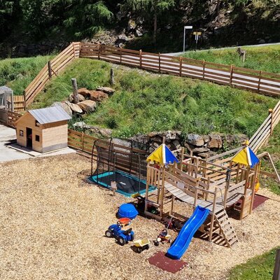 Der Kinderspielplatz des Bauernhofs umfasst eine Holzspielstruktur mit Rutsche, ein Trampolin und ein kleines Spielhaus auf Hackschitzel-Boden.