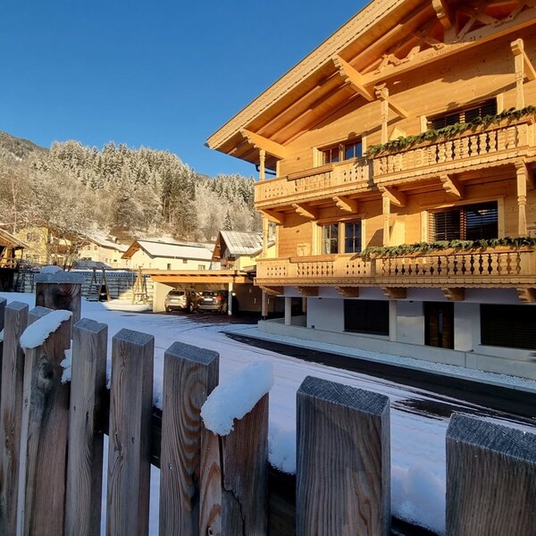 Außenansicht des Bauernhofs mit Holzbalkonen, Carport und schneebedeckter Landschaft im Winter.