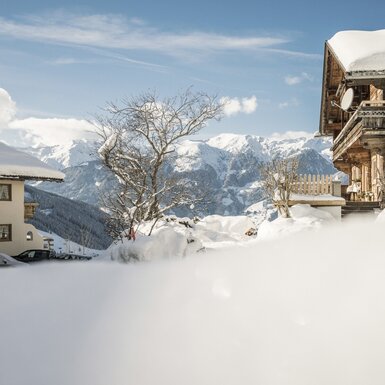 Der Bauernhof Hanscherhof und ein traditionelles Holzhaus, umgeben von Schnee mit Bergblick und einem Parkplatz.