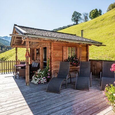 Die Holzhütte auf dem Bauernhof mit Holzterrasse, ausgestattet mit Liegestühlen und Sitzgelegenheiten, bietet einen Ausblick auf die grüne Hügellandschaft.