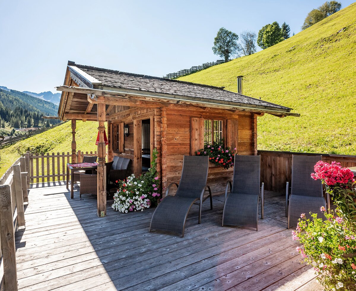 Die Holzhütte auf dem Bauernhof mit Holzterrasse, ausgestattet mit Liegestühlen und Sitzgelegenheiten, bietet einen Ausblick auf die grüne Hügellandschaft.