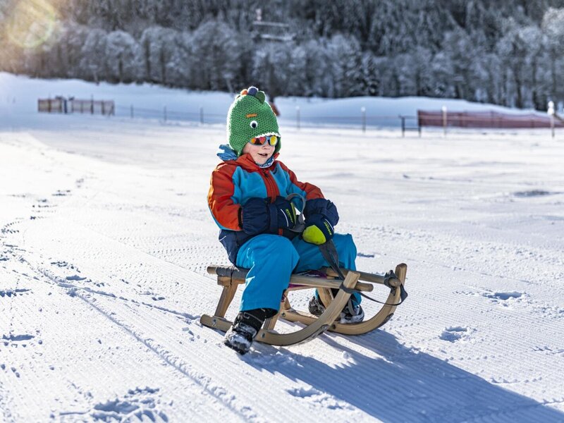Ein Kind auf einem Schlitten im Schnee, eine Winteraktivität für Gäste am Bauernhof.