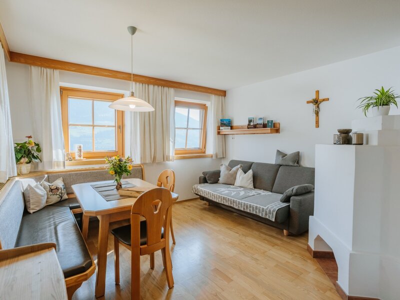 Geräumiges Wohnzimmer der Ferienwohnung im Bauernhof mit Esstisch, Ausziehcouch und traditionellem Bauernofen.