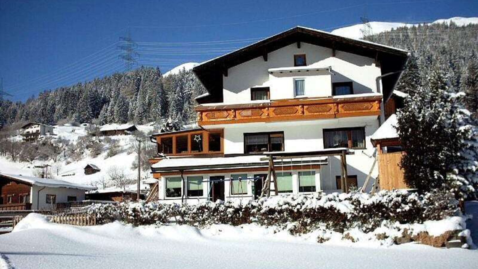 Der Bauernhof von außen, mit Balkon und Wintergarten, umgeben von Schnee.