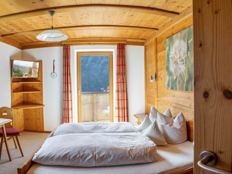 Schlafzimmer im Bauernhof mit zwei Einzelbetten, Holzvertäfelung, TV und Zugang zum Balkon.