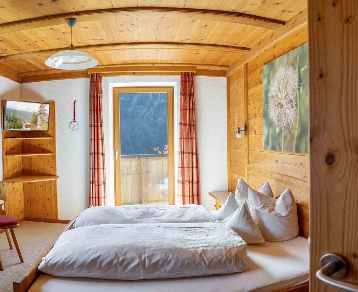 Schlafzimmer im Bauernhof mit zwei Einzelbetten, Holzvertäfelung, TV und Zugang zum Balkon.