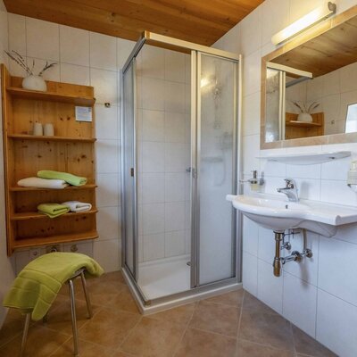 Badezimmer im Bauernhof mit Duschkabine, Waschbecken, Spiegel und Holzregal für Handtücher.