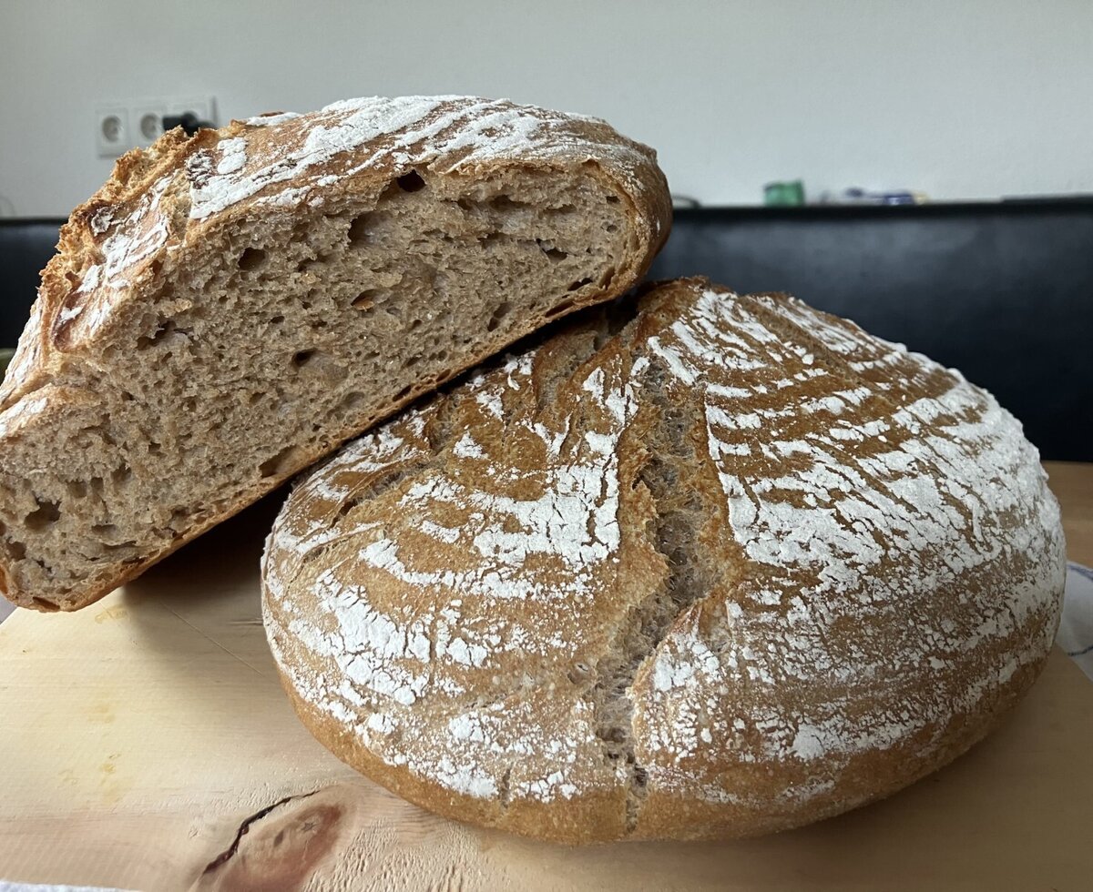 Hausgemachtes Bauernbrot, mit einem ganzen Laib und einer angeschnittenen Hälfte, präsentiert auf einem Holzbrett.