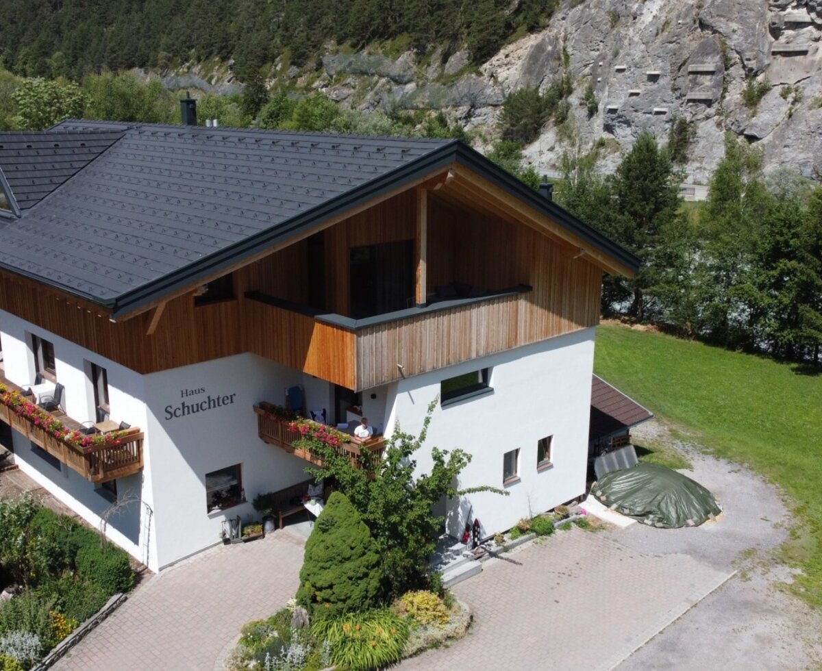Außenansicht des Bauernhofs 'Haus Schuchter' mit Garten und Berglandschaft.
