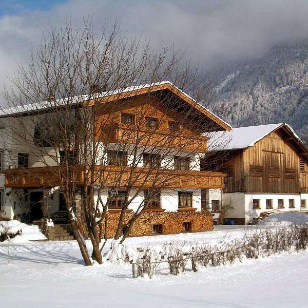Außenansicht des Bauernhofs mit Holzbalkonen und schneebedeckter Umgebung vor einer Bergkulisse.