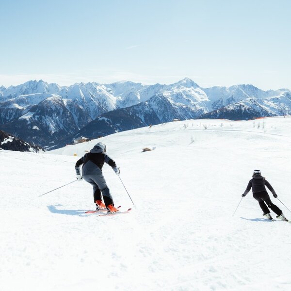 Zwei Personen beim Skifahren auf einer verschneiten Piste mit Bergpanorama.
