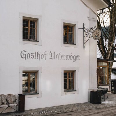 Außenansicht des Gasthof Unterwöger mit Beschriftung, Fenstern und einem Sitzbereich im Freien.