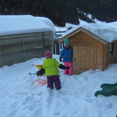 Spielbereich für Kinder mit Holzspielhaus und Rutsche im Schnee auf dem Bauernhof.