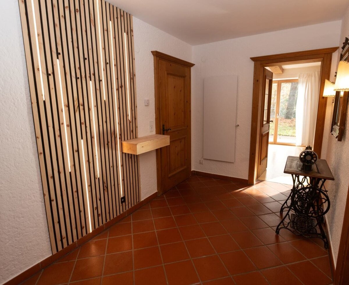 Eingangsbereich des Apartments mit moderner Holzlamellenwand, integrierter Beleuchtung und Terrakottafliesen.
