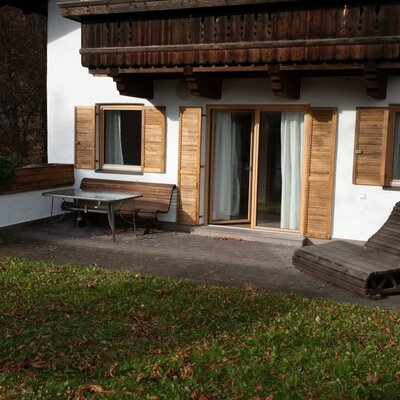 Die private Terrasse des Apartments bietet einen Esstisch, eine Bank, eine Holzliege und direkten Zugang zu einer Rasenfläche.