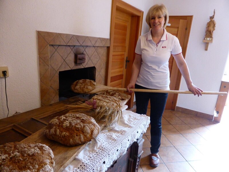 Die Gastgeberin präsentiert frisch gebackenes Brot aus dem traditionellen Ofen des Bauernhofs.