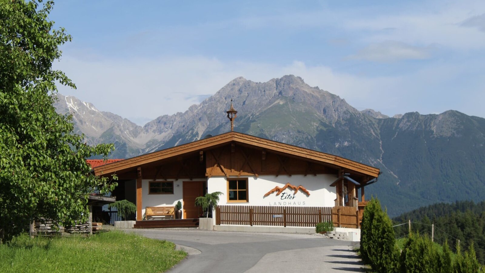 Das Äußere der Ap­par­te­ments im Landhausstil mit Bergkulisse und Zufahrt.