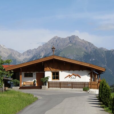 Das Äußere der Ap­par­te­ments im Landhausstil mit Bergkulisse und Zufahrt.