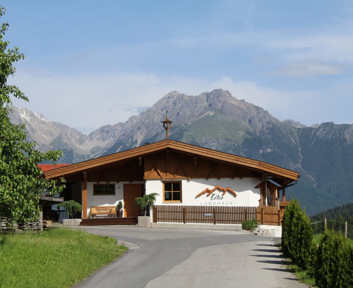 Das Äußere der Ap­par­te­ments im Landhausstil mit Bergkulisse und Zufahrt.