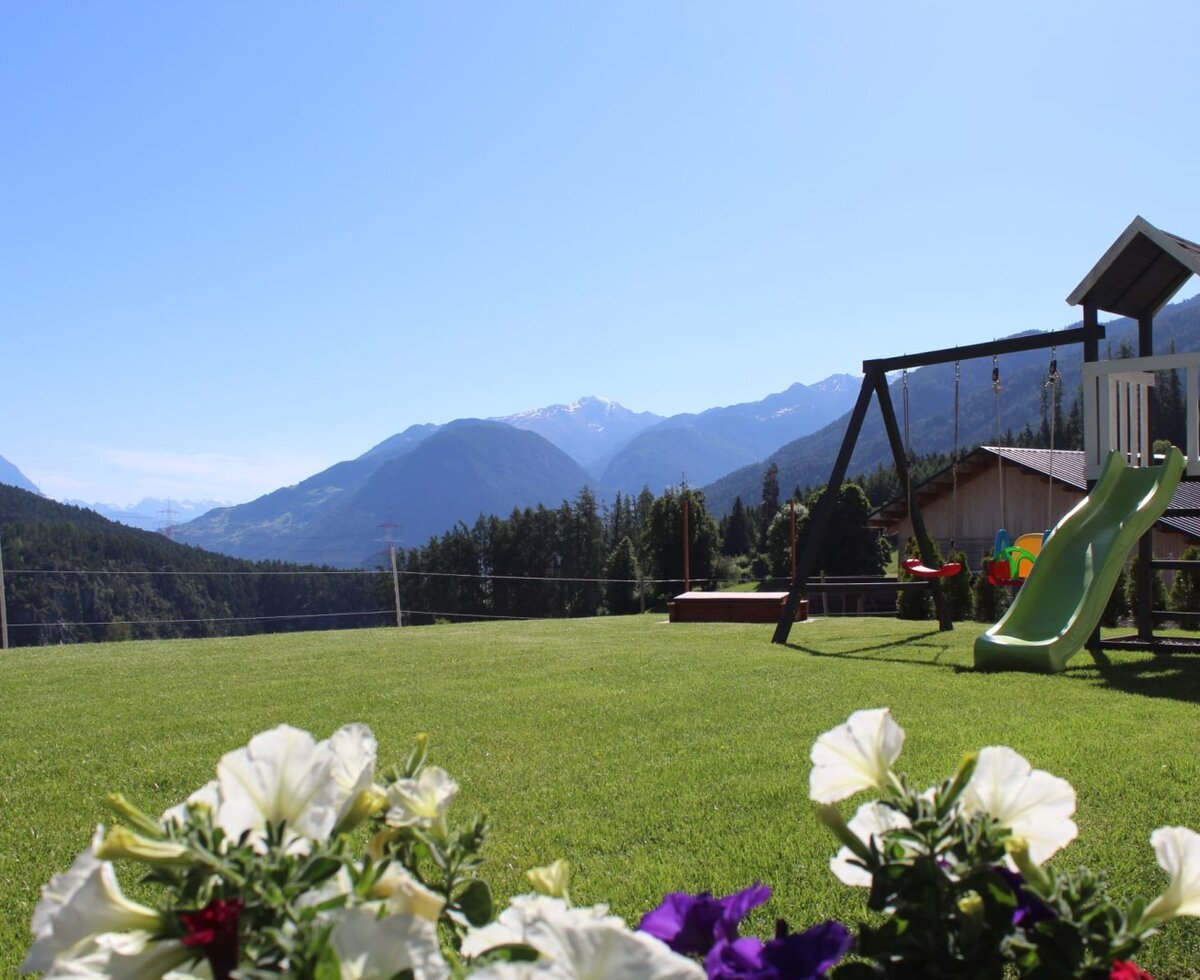 Grüne Wiese mit Kinderspielplatz und Bergblick, Teil der Ap­par­te­ments.