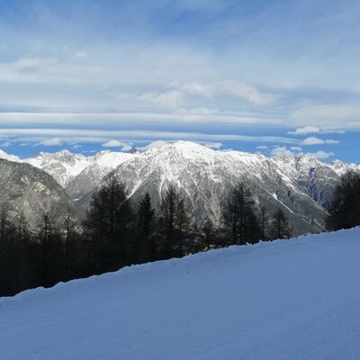 Winterlicher Blick auf die schneebedeckten Berge und eine Skipiste vom Bauernhof.