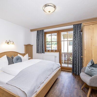 Doppelzimmer im Bauernhof mit Holzbett, Kleiderschrank und Balkonzugang.