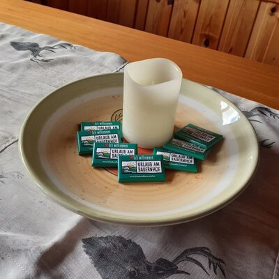 Eine Kerze und "Urlaub am Bauernhof" Schokoladen als Willkommensgruß auf einem Tisch in der Alm.