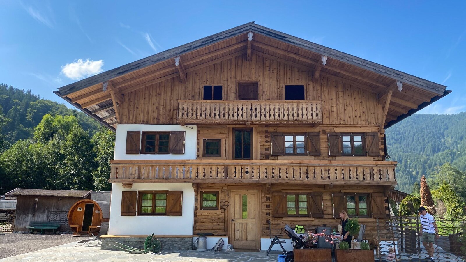 Das Bauernhofgebäude mit Holzbalkonen, Fenstern mit Holzläden, umgeben von Bergen.