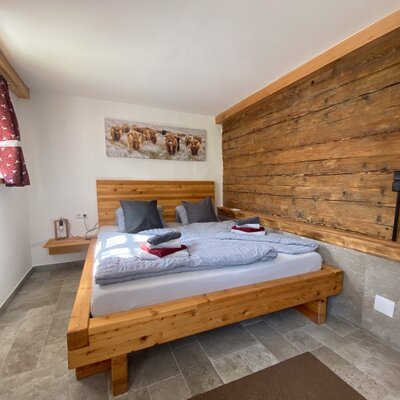 Schlafzimmer im Bauernhof mit einem Doppelbett aus Holz, einer Holzwand und Fliesenboden.