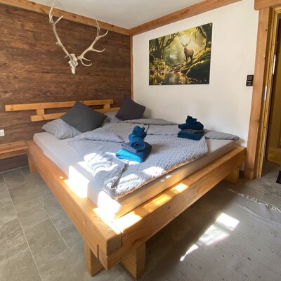 Schlafzimmer im Bauernhof mit Doppelbett, Holzwandverkleidung und Hirschgeweih.