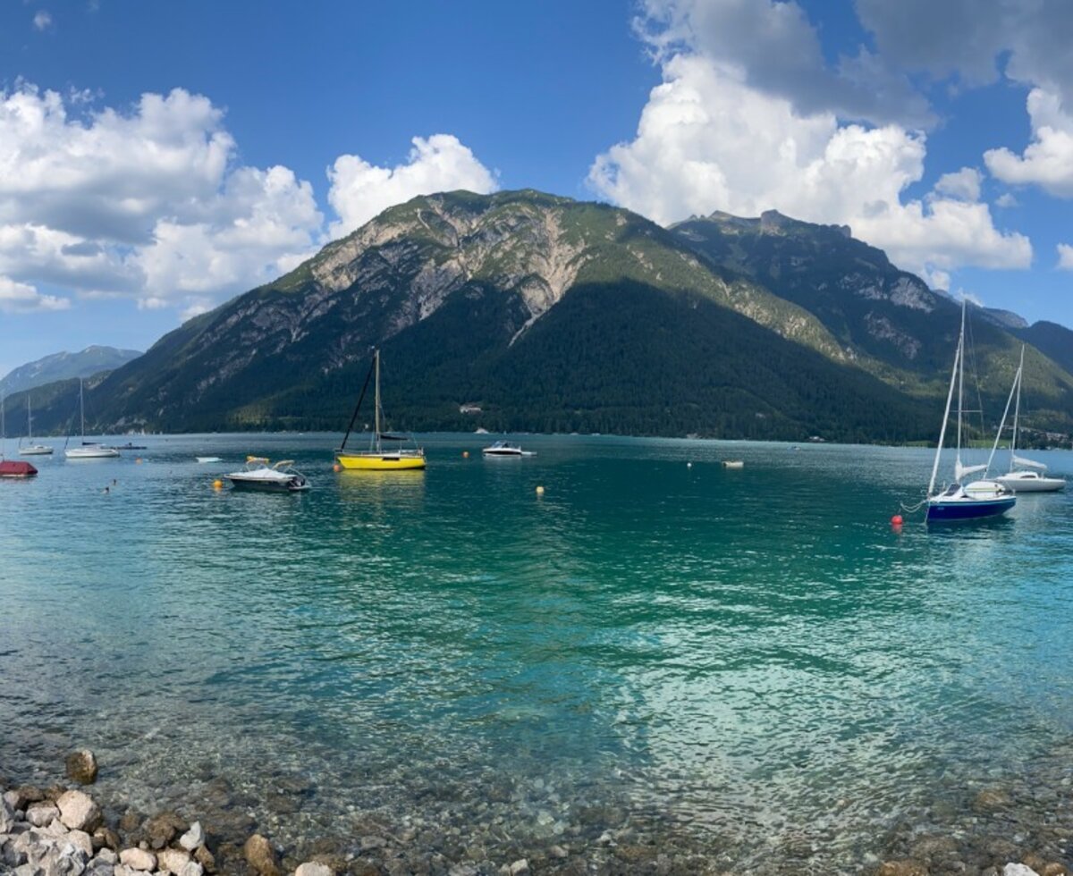 Der Achensee mit Segelbooten, Badegästen und umliegenden Bergen bietet Freizeitmöglichkeiten für Gäste des Bauernhofs.